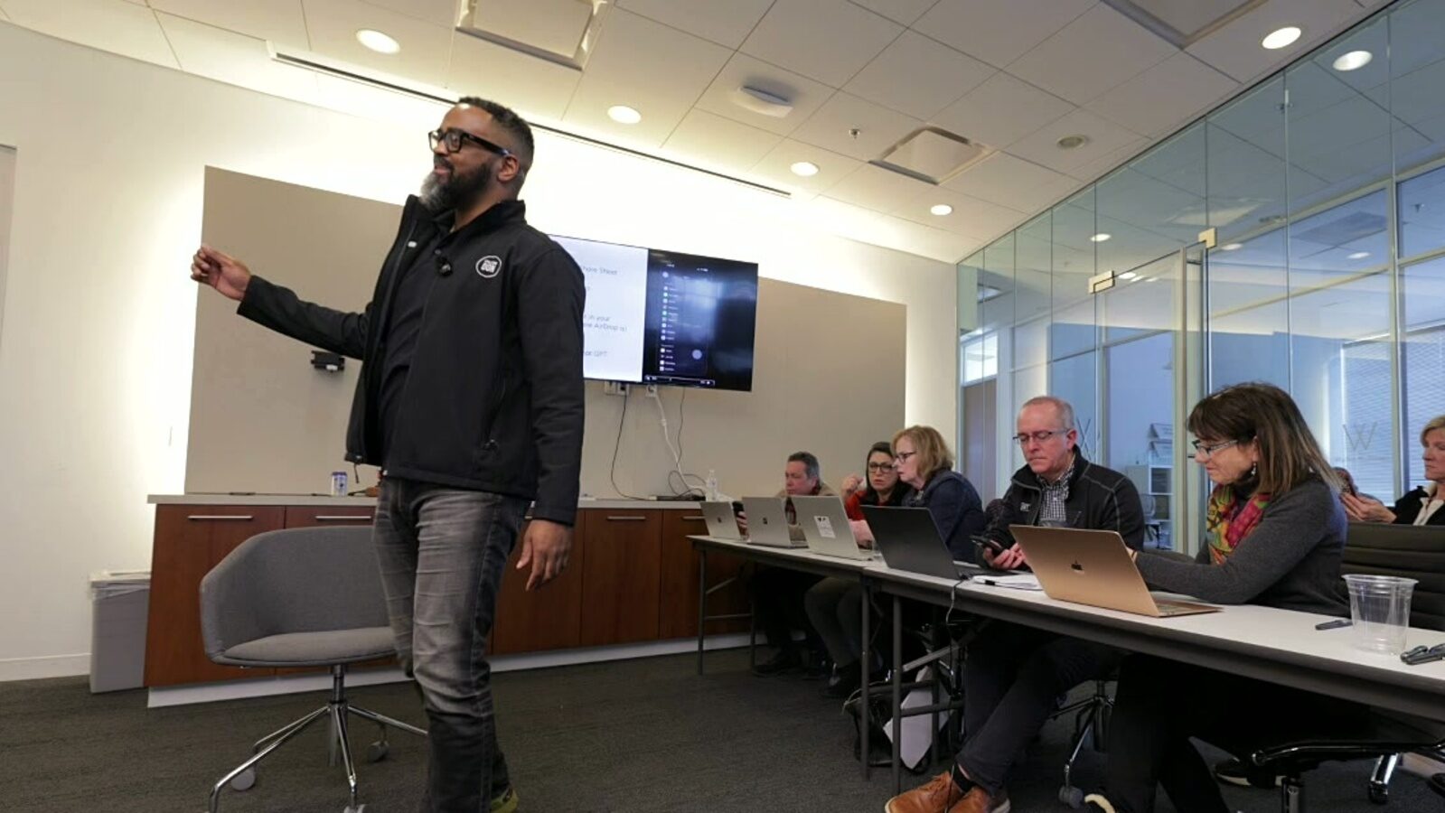 Donald Gray presenting at the front of a conference room while attendees follow along on laptops.