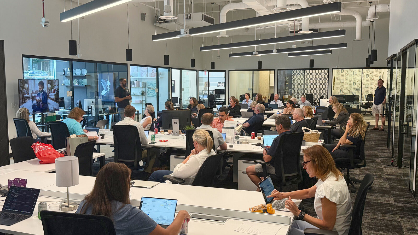 Donald Gray II teaching a packed AI class in a bright, modern open workspace, attendees following along on laptops.